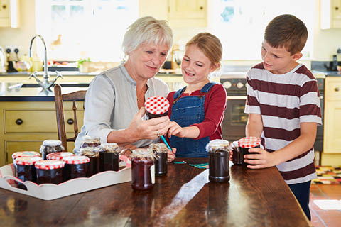 Eine Großmutter kocht mit ihren Enkelkindern Marmelade ein.
