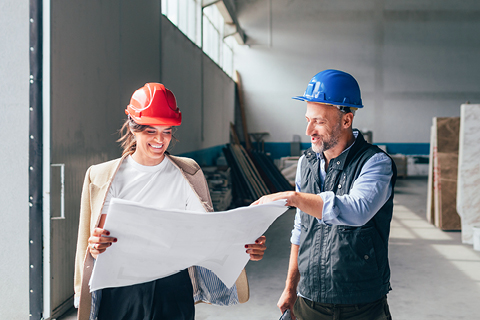 Ein Mann und eine Frau mit Bauhelm stehen auf einer Baustelle und studieren einen Plan.