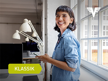 Eine junge Frau steht vor einer Fensterfront im Büro und hält lachend ihr Handy in der Hand.