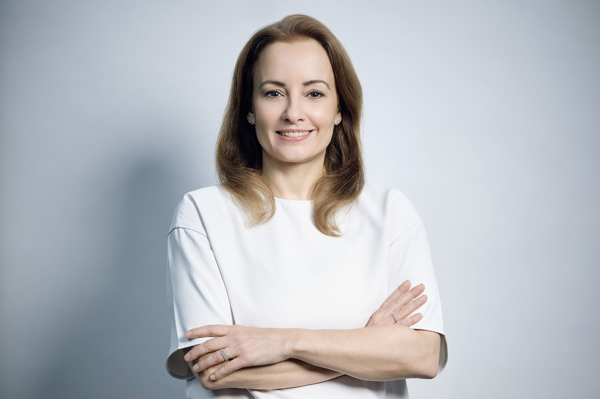 Christine Reuters mit verschränkten Armen auf hellblauem Hintergrund.