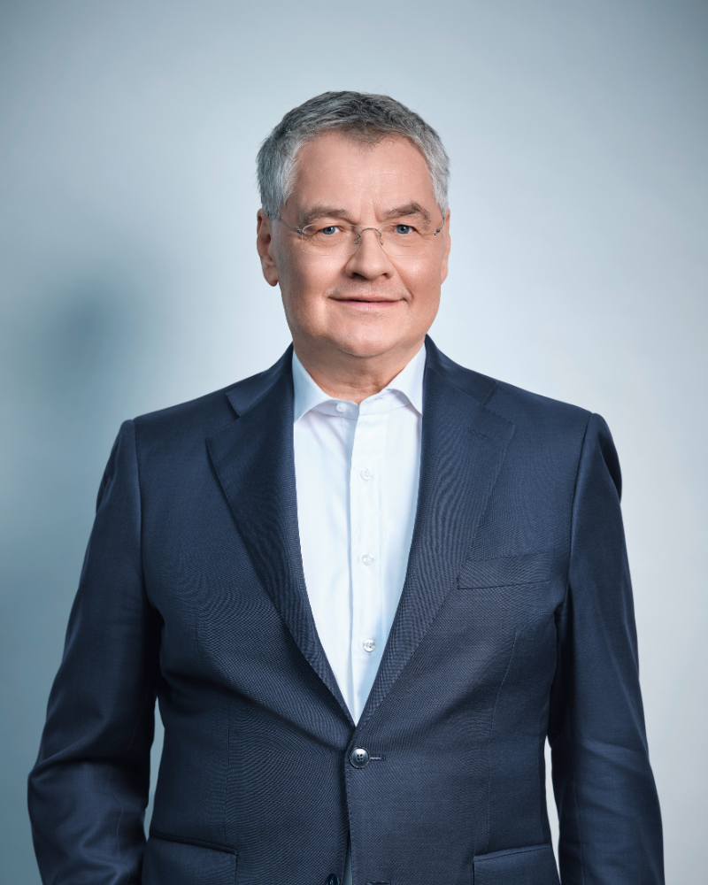Thomas Uher im Anzug auf hellblauem Hintergrund.