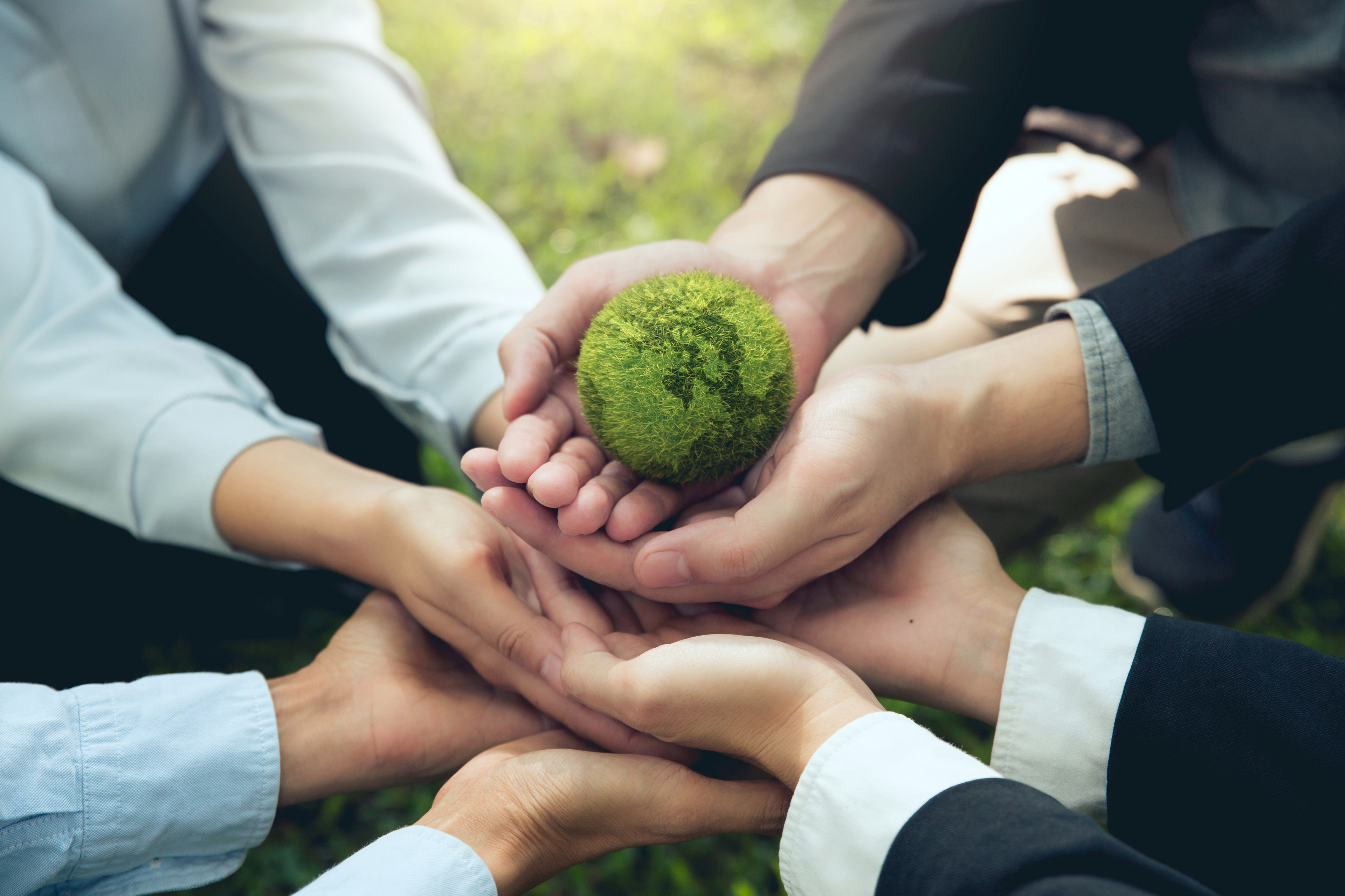 Viele Menschen haben ihre Hände zusammen in die Mitte gelegt und halten einen grünen Ball, der die Erde symbolisiert.