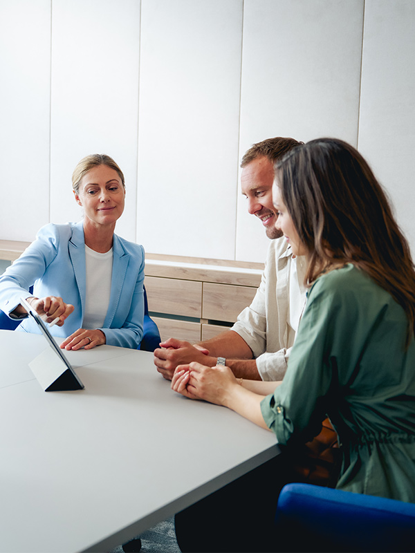 Eine Frau im Blazer berät ein Paar und zeigt ihnen etwas auf einem Laptop.
