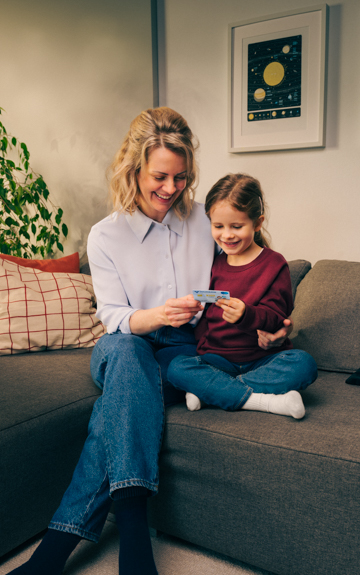 Mutter und Tochter sitzen auf der Couch und betrachten gemeinsam eine Volksbank Jugend Sparkarte.