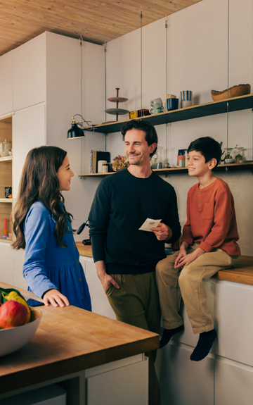 Eine junge Familie befindet sich in der Küche. Der Sohn sitzt auf der Arbeitsfläche, der Vater hält ein Stück Papier in der Hand.