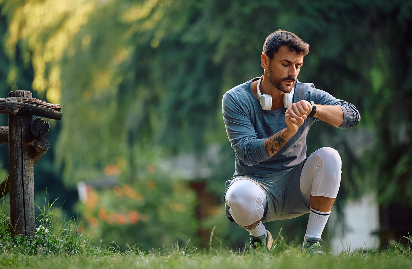 Ein Mann in Sportkleidung und mit Kopfhörern um den Hals ist in der Hocke und bedient seine Smart-Watch.