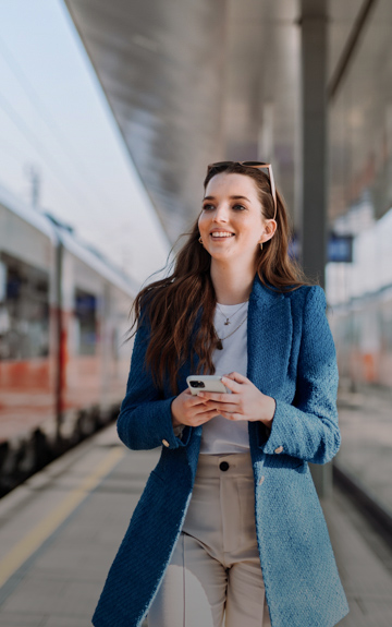Eine Frau geht auf dem Bahnsteig. Sie hat ein Mobiltelefon in der Hand.