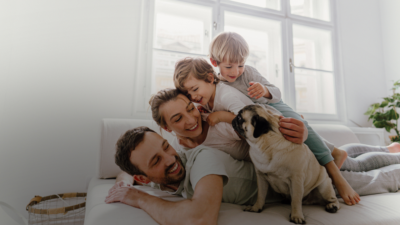 Eine Familie liegt auf der Couch: Der Vater ganz unten, darüber eine Frau und zwei Kinder und daneben ein Mops.