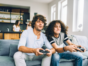 Zwei Personen sitzen auf einer Couch und spielen auf einer Spielkonsole.