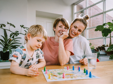 Zwei Frauen und ein Kind sitzen an einem Tisch und spielen ein Brettspiel.