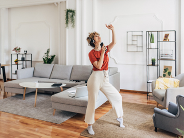 Eine Frau ist in ihrer Wohnung. Sie hat Kopfhörer auf und tanzt zur Musik von ihrem Mobiltelefon.